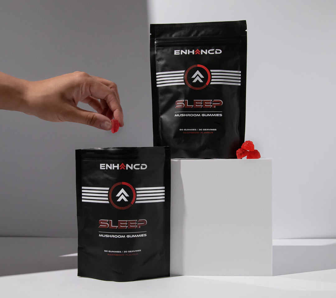 Two black ENHANCD sleep mushroom gummies packages with a hand holding a gummy.