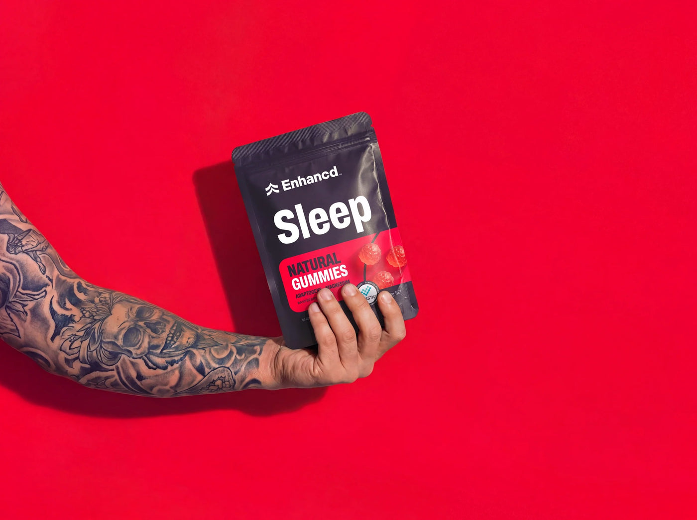 A hand holding a pouch of Enhancd Sleep Gummies against a red background
