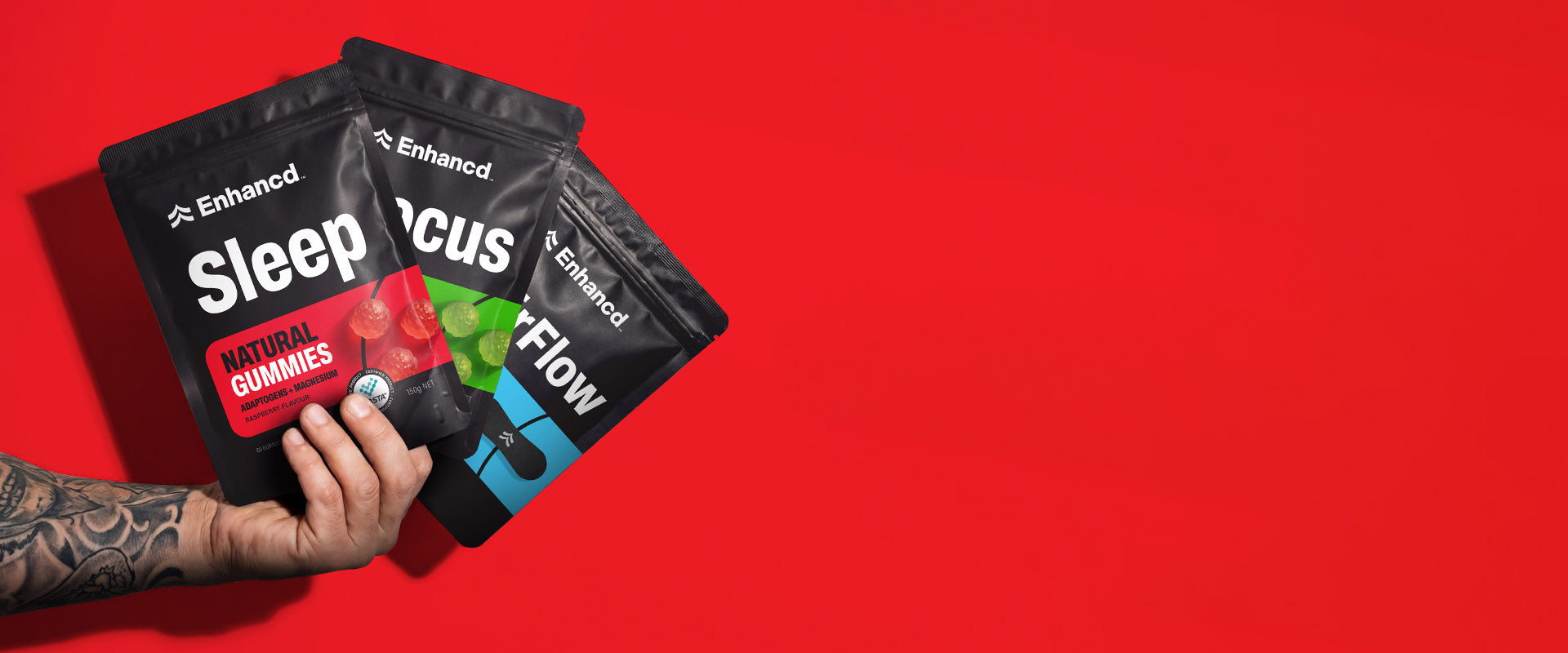 Hand holding three 'Enhanced' supplement packages against a red background