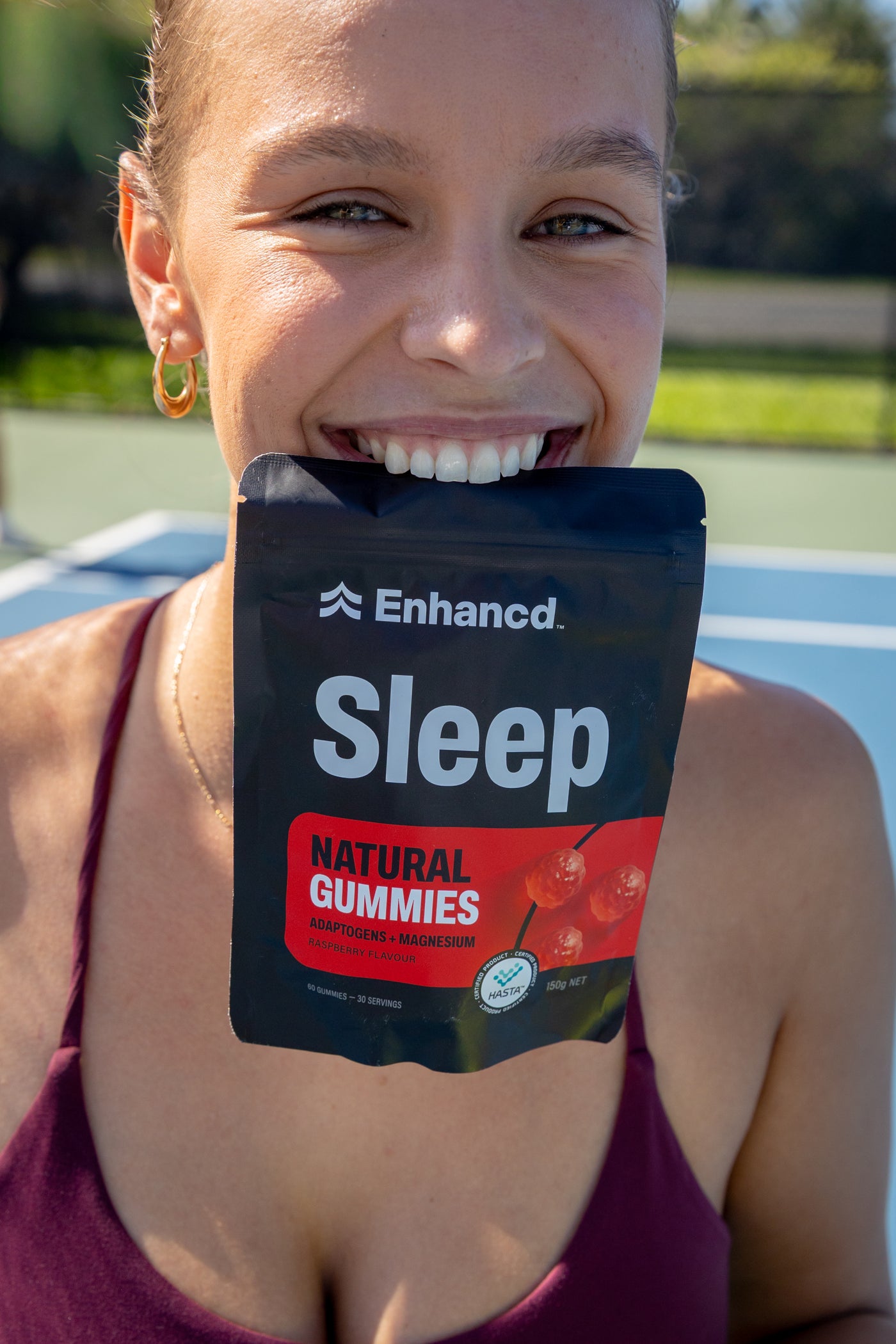 Woman holding an Enhancd Sleep pouch on a tennis court