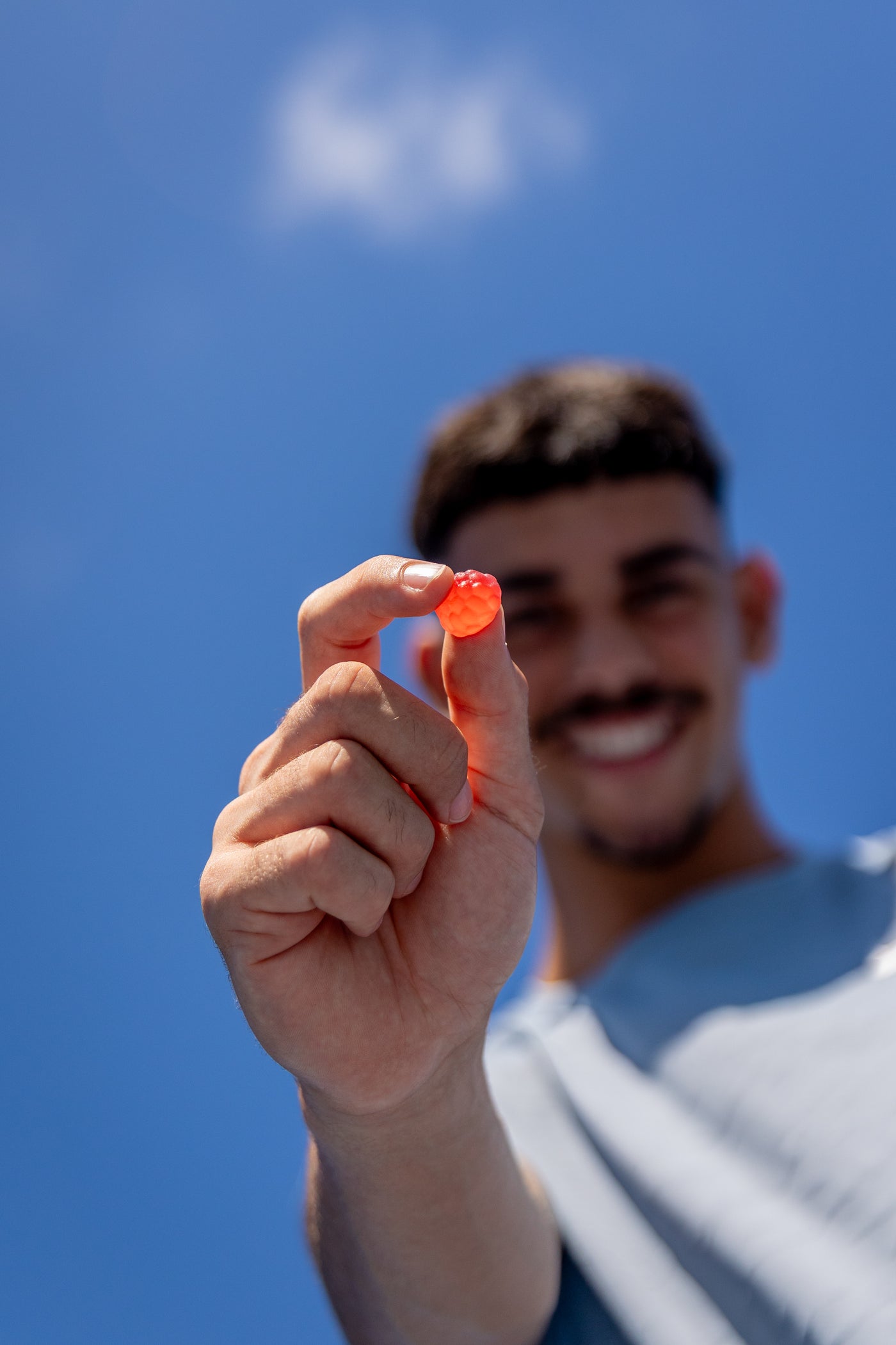 Man smiling and holding an Enhancd Sleep raspberry gummy