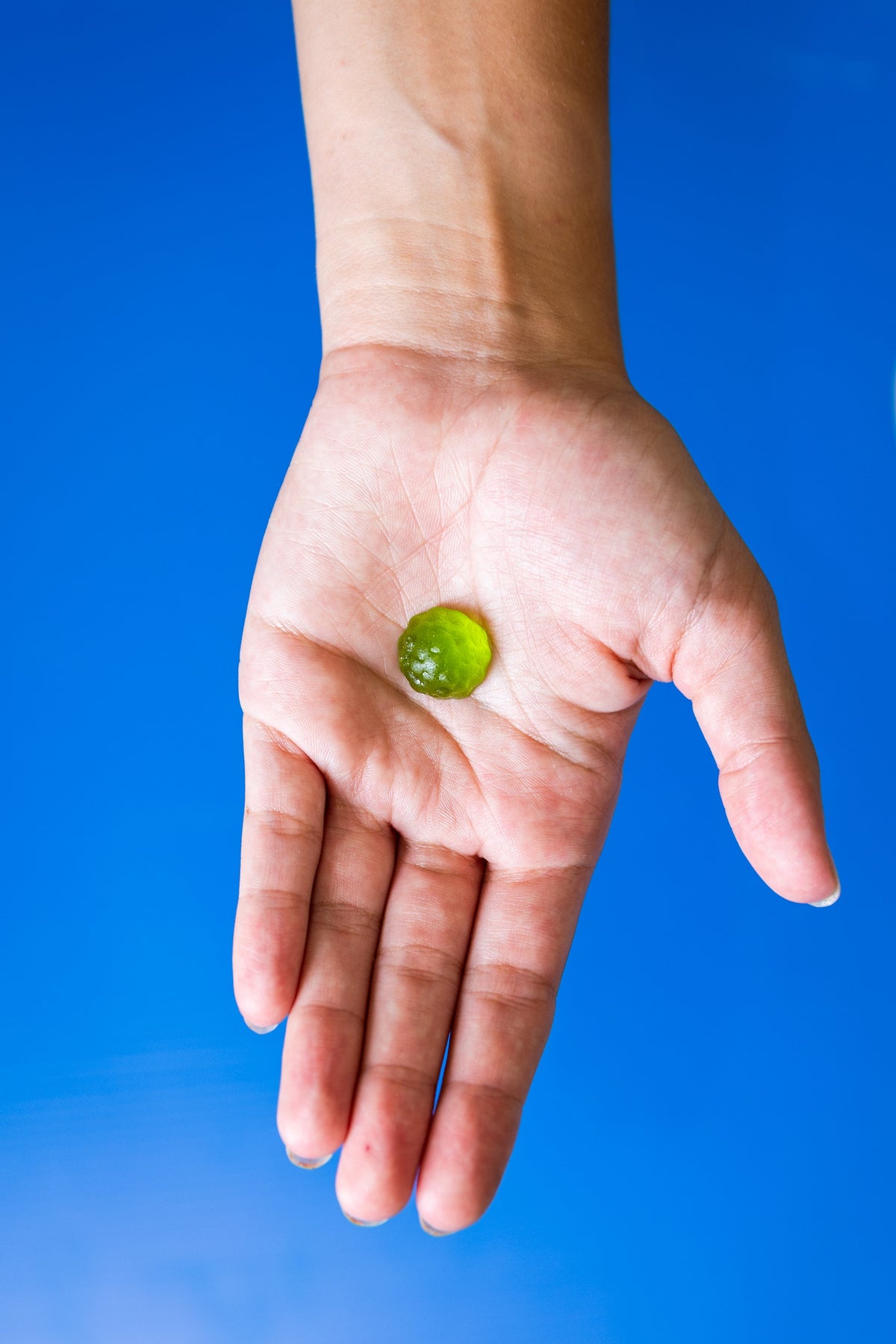 Hand holding an Enhancd Focus apple gummy against a blue background