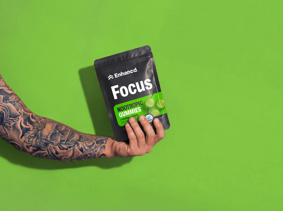 A hand holding a pouch of Enhancd Focus Gummies against a green background